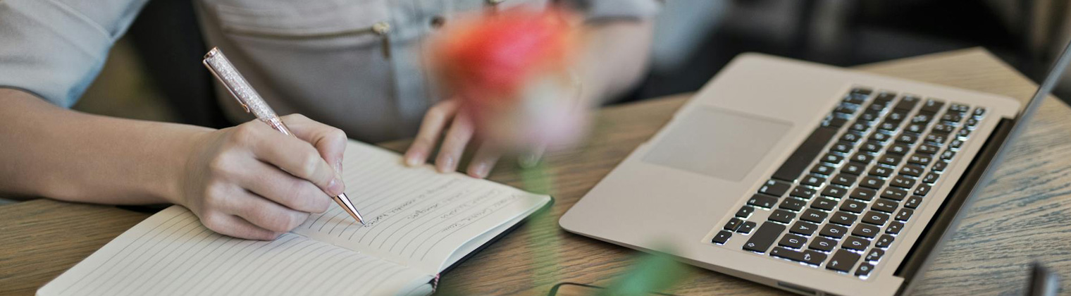 Image of a professional content writer writing down notes for his blog with his laptop open